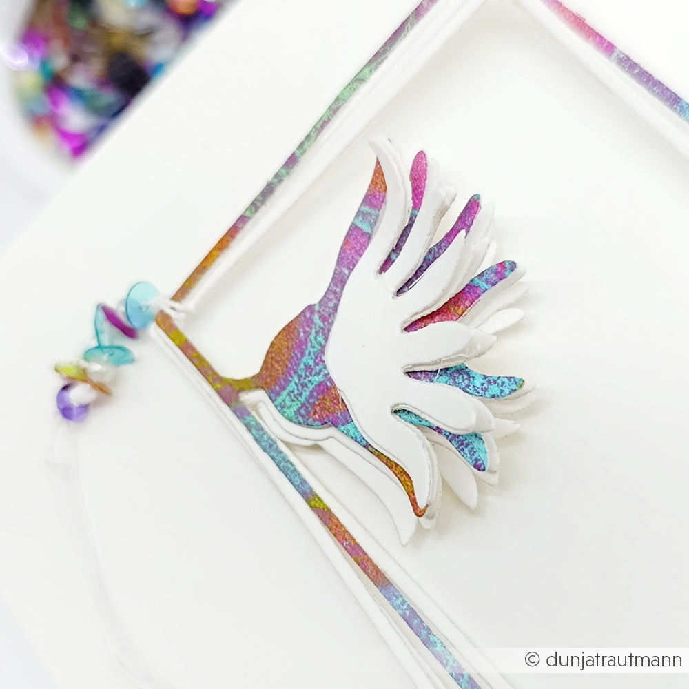 Nahaufnahme eines farbenfrohen, holografischen vogelförmigen Papierkunstwerks mit Perlen auf weißem Hintergrund, hergestellt mit Alexandra Renke Deep Edge Motivstanzen für präzise Details.