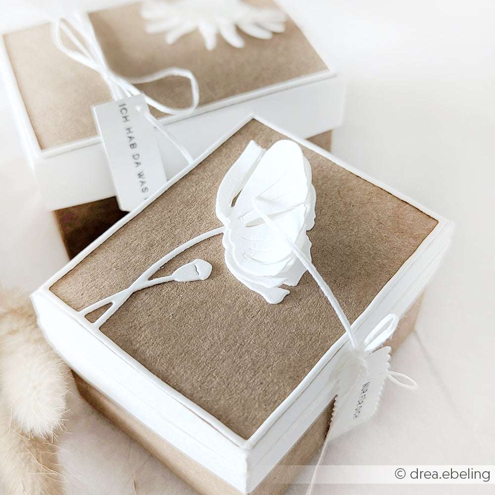 Zwei braun-weiße Geschenkschachteln, verziert mit weißen Papierblumen und Anhängern, verschnürt mit weißer Schnur - hergestellt mit Alexandra Renke Deep Edge Motivstanzen für scharfe Kanten und einzigartige Designs.