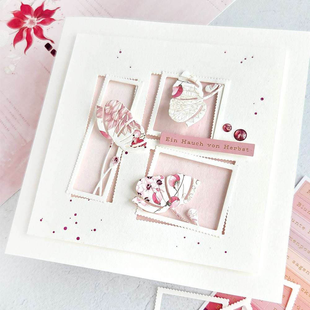 Handgefertigte Karte mit rosafarbenen und weißen Blättern, die mit Alexandra Renkes Motivstanze Mohn im Rahmen gestaltet wurden, akzentuiert mit deutschem Text und rosa Farbspritzern auf weißem Hintergrund.