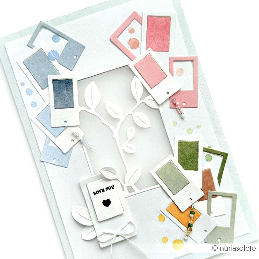 Handgemachte Karte mit bunten Polaroid-Rahmen, Blättern, die mit der Motivstanze Zweig im Rahmen von Alexandra Renke geschnitten wurden, und einem kleinen Anhänger mit der Aufschrift LOVE YOU und einem Herz.