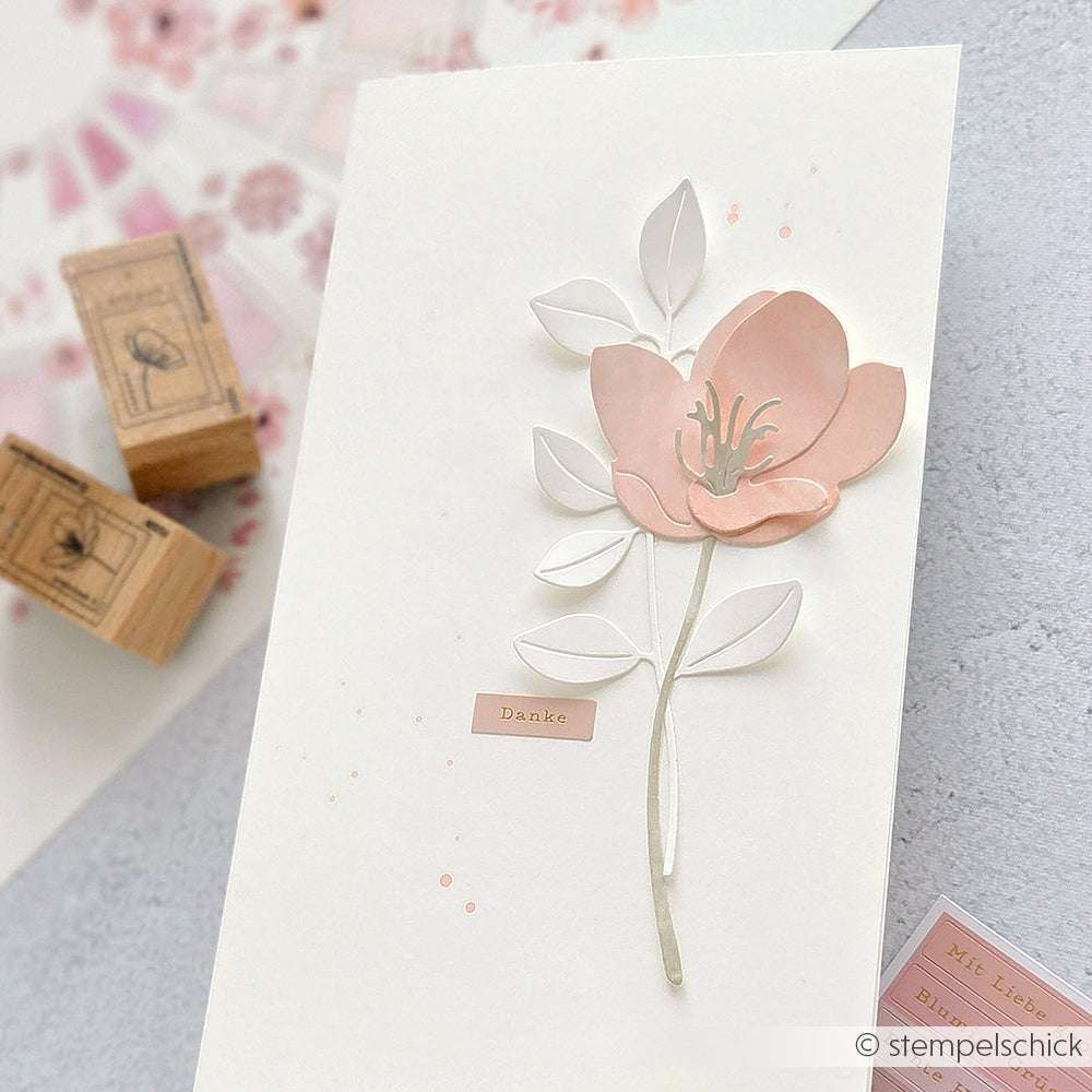 Eine weiße Karte von Alexandra Renke, die mit PAPPcut®ies Deep Edge Stanzen mit einem rosafarbenen Blumen- und Blättermotiv verziert wurde, trägt ein Etikett mit "Danke" in goldenen Buchstaben.