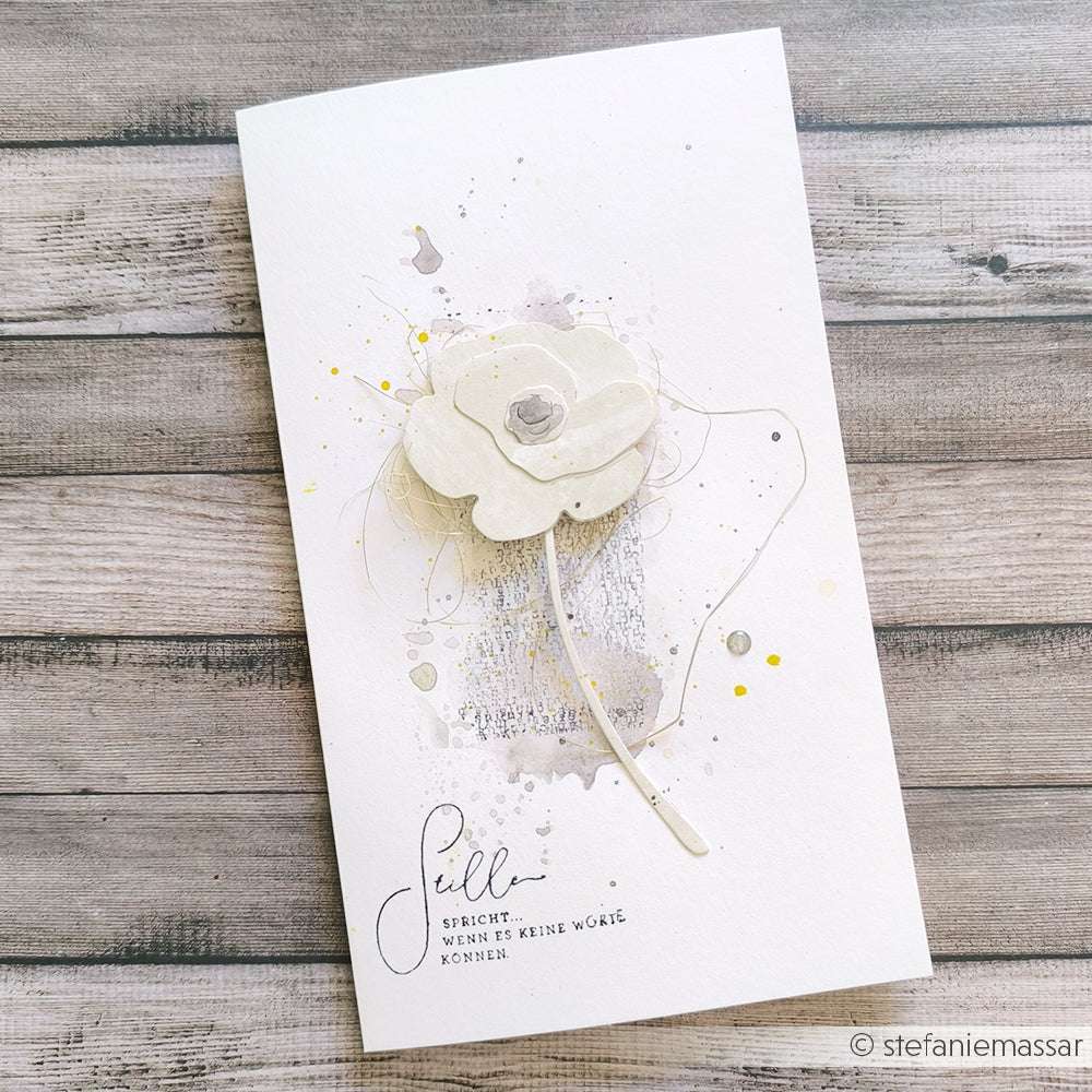 Eine handgefertigte Karte von Alexandra Renke mit einer weißen 3D-Blume, hergestellt mit Motivstanze und Deep Edge Stanzen, mit deutschem Text auf einem hellen Holzhintergrund.
