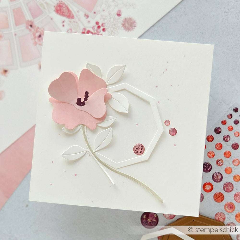 Eine weiße Karte mit einer rosafarbenen Papierblume, geometrischen Formen und zarten Blättern auf einem pastellfarbenen Hintergrund, gestaltet mit Alexandra Renke Motivstanze Geschwungene Blüte.