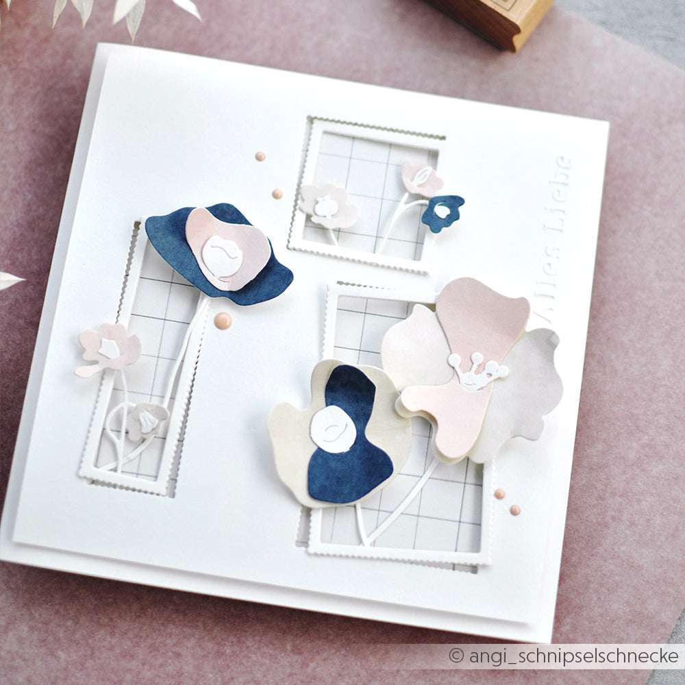 Eine weiße Karte mit pastellfarbenen und marineblauen Papierblumen, ausgeschnittenen Fensterrahmen, die mit Alexandra Renke Deep Edge Stanzen hergestellt wurden, und einem Gitterhintergrund.