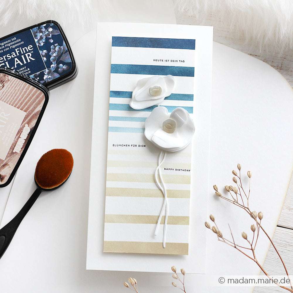 Handgemachte Geburtstagskarte mit ombré blauen und beigen Streifen, hergestellt mit Alexandra Renke Deep Edge Stanzen für klare Linien und zwei weißen 3D-Blumen auf weißem Hintergrund.