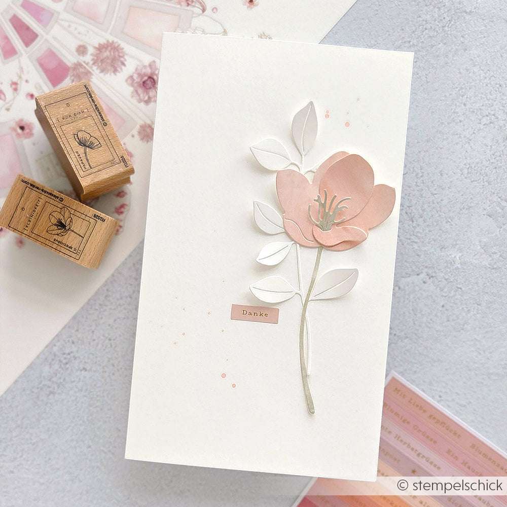 Handgefertigte Karte mit einer rosafarbenen 3D-Blume, Blättern und einem Danke-Etikett, erstellt mit Alexandra Renke Deep Edge Stanzen PAPPcut®ies Motivstanze, abgebildet neben dekorativen Holzstempeln.