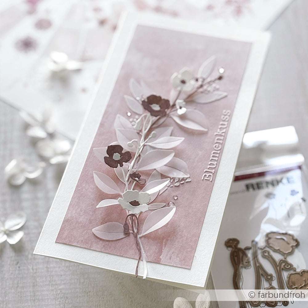 Handgemachte Karte mit 3D-Papierblumen und Blättern auf rosa Hintergrund, hergestellt mit Alexandra Renke PAPPcut®ies und Deep Edge Motivstanzen. "Blumenkuss" ist elegant in weißer Schrift geschrieben.