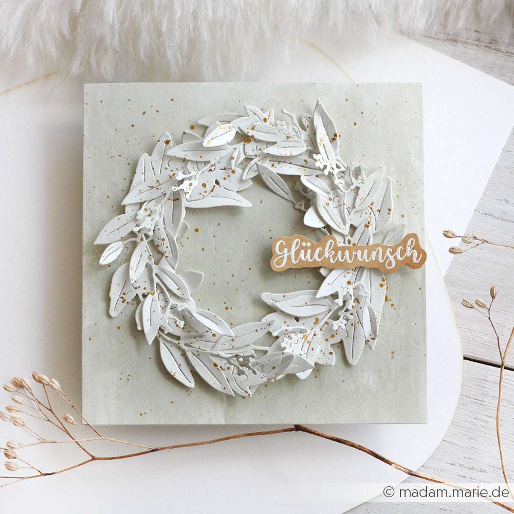 Eine handgefertigte Karte von Alexandra Renke zeigt einen weißen Papierkranz aus PAPPcut®ies und der Motivstanze Feines Beerenzweig-Trio, veredelt mit einem goldenen Glückwunsch-Zeichen auf hellem Hintergrund.
