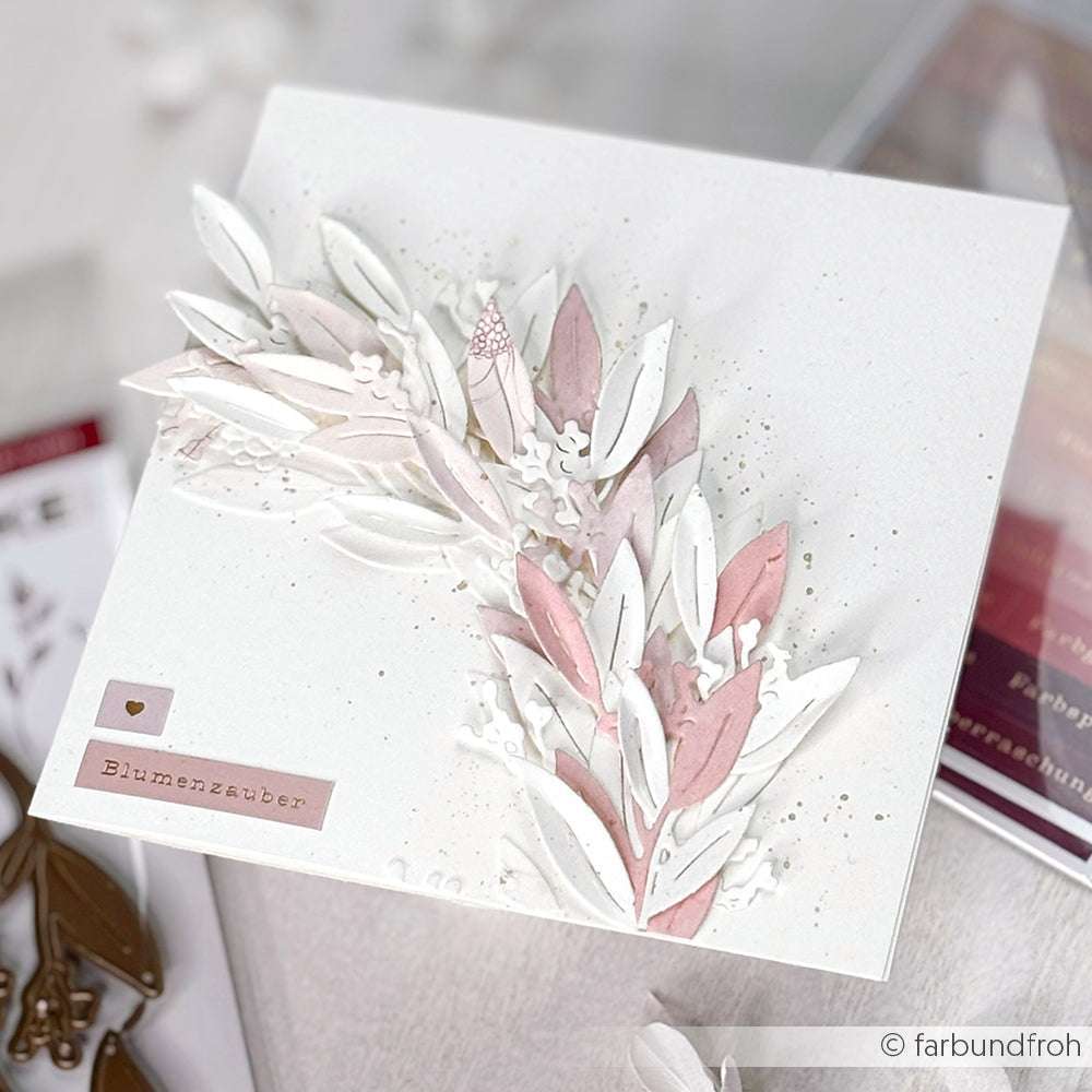 Handgefertigte weiße Grußkarte von Alexandra Renke mit geschichteten rosa und weißen Papierblättern, die mit Deep Edge Stanzen und PAPPcut®ies hergestellt wurden, und einem Blumenzauber-Etikett auf der Vorderseite.