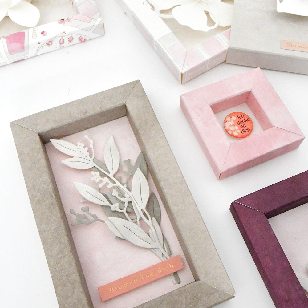 Dekorative Papierrahmen mit floralen Motiven und deutschem Text, hergestellt mit der Motivstanze Beerenzweig von Alexandra Renke, sind wunderschön auf einer weißen Fläche angeordnet.