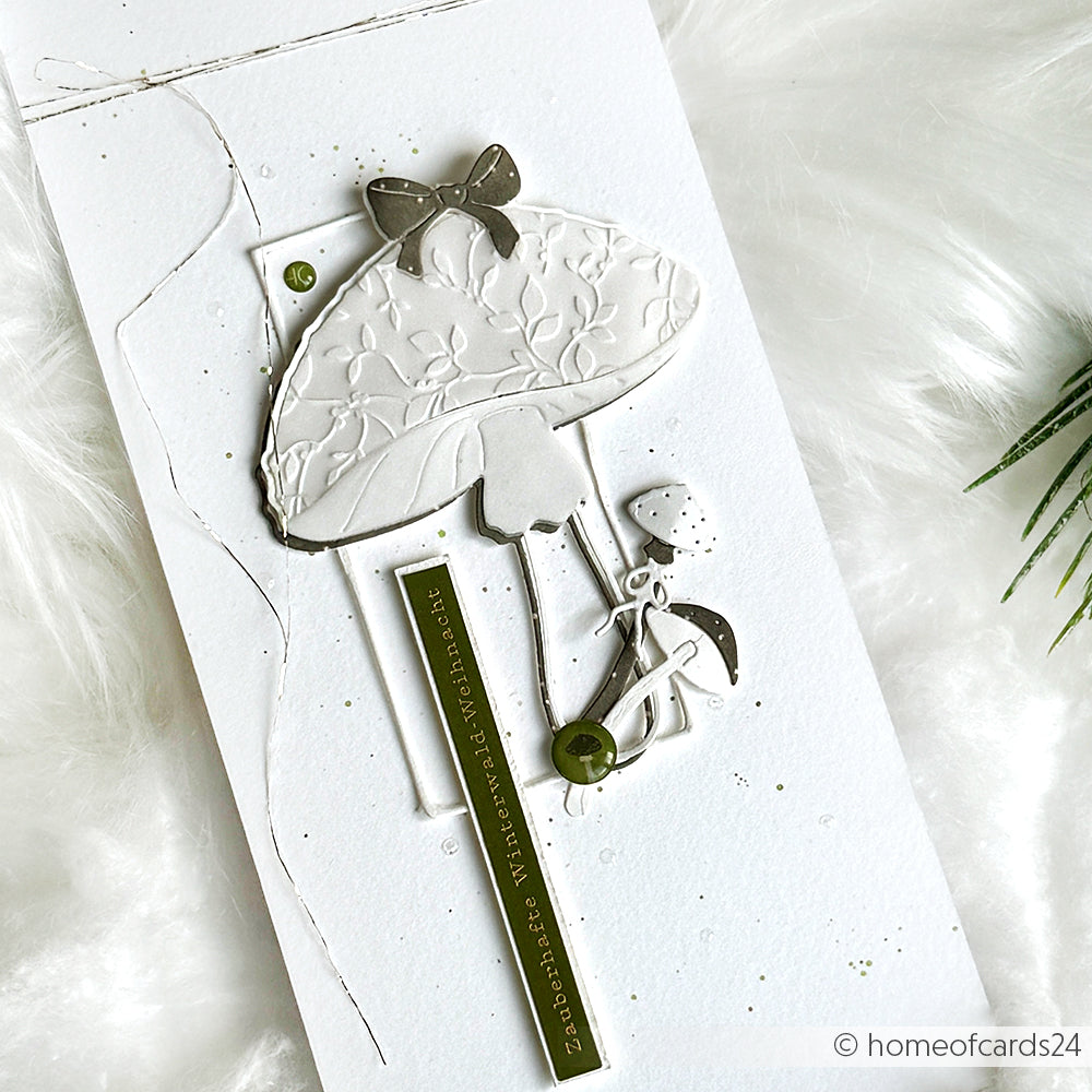Handgefertigte Karte mit einem geprägten weißen Pilz, der mit der Motivstanze Freudenpilz von Alexandra Renke gestaltet wurde, einem kleinen Blatt, einem Band und grünen Akzenten auf Weiß - ideal, um Ihre Lieblingsdesignpapiere zu präsentieren.