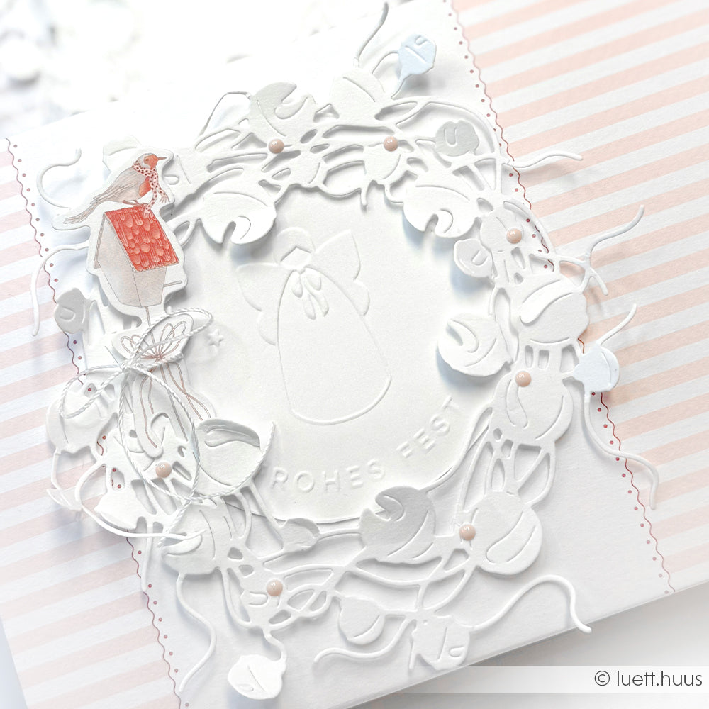 Die weiße Karte von Alexandra Renke zeigt einen zarten Motivstanze-Glöckchenkranz, einen Engelsumriss, den Text Frohes Fest" und ein Mädchen in einem roten Kleid auf pastellfarben gestreiften Designpapieren.