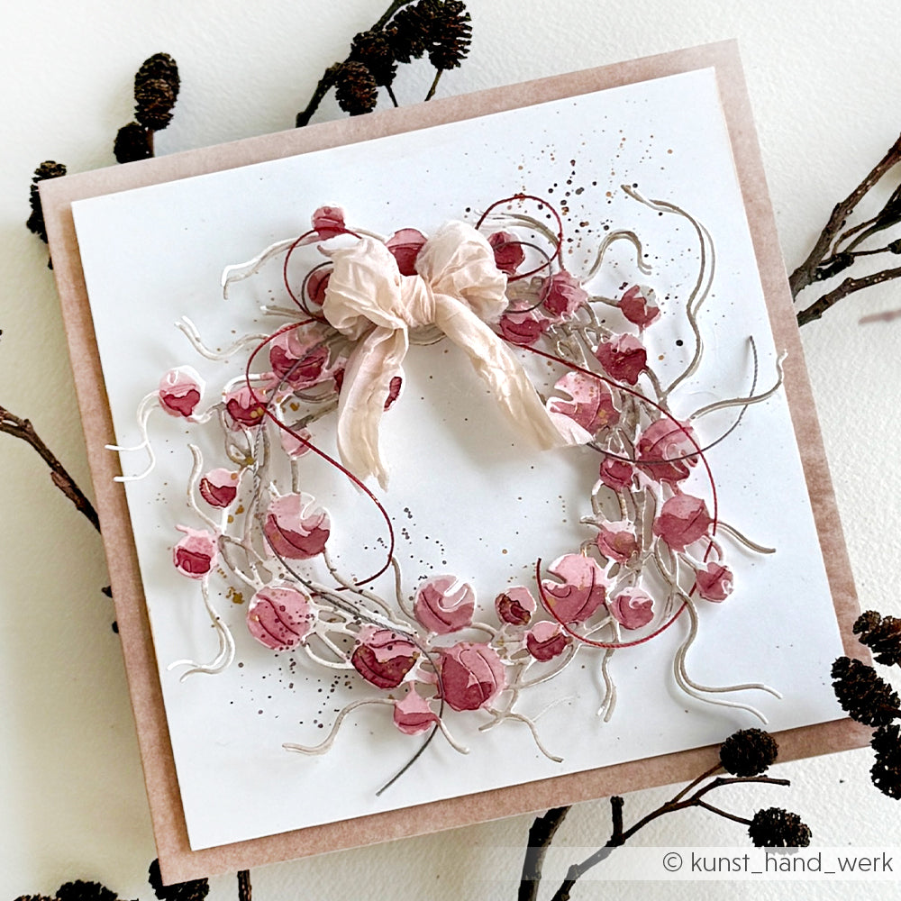 Handgefertigte Karte von Alexandra Renke mit rosafarbenem und rotem Blumenkranz, einer Stoffschleife, zarten Zweigen, elegantem edle Designpapier und der Motivstanze Glöckchenkranz für einen edlen Look.