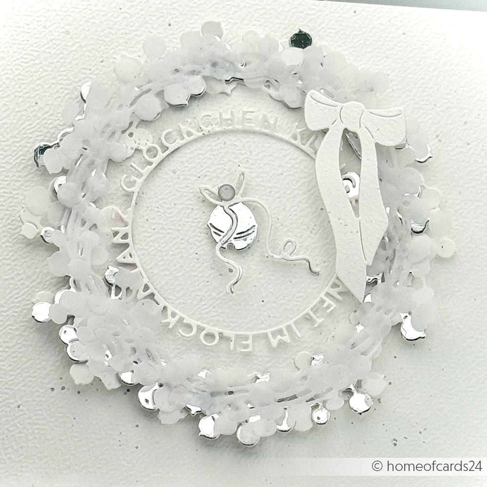 Weiße Blumenkranzkarte mit Schleife, Pailletten und Garnkugel auf strukturiertem Papier, mit kreisförmigem ungarischen Text. Hergestellt mit der Motivstanze Großer Beerenkranz von Alexandra Renke und eleganten Designpapier Stanzen für ein detailreiches Finish.