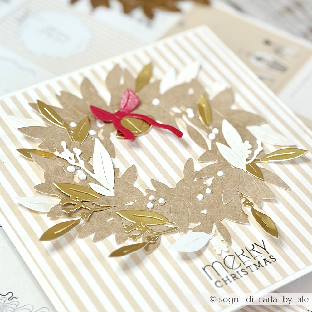 Handgefertigte Weihnachtskarte von Alexandra Renke mit einem goldenen, weißen und braunen Kranz aus Motivstanze Blätterkranz, einer roten Schleife und dem Text "Frohe Weihnachten" auf elegantem Designpapier.