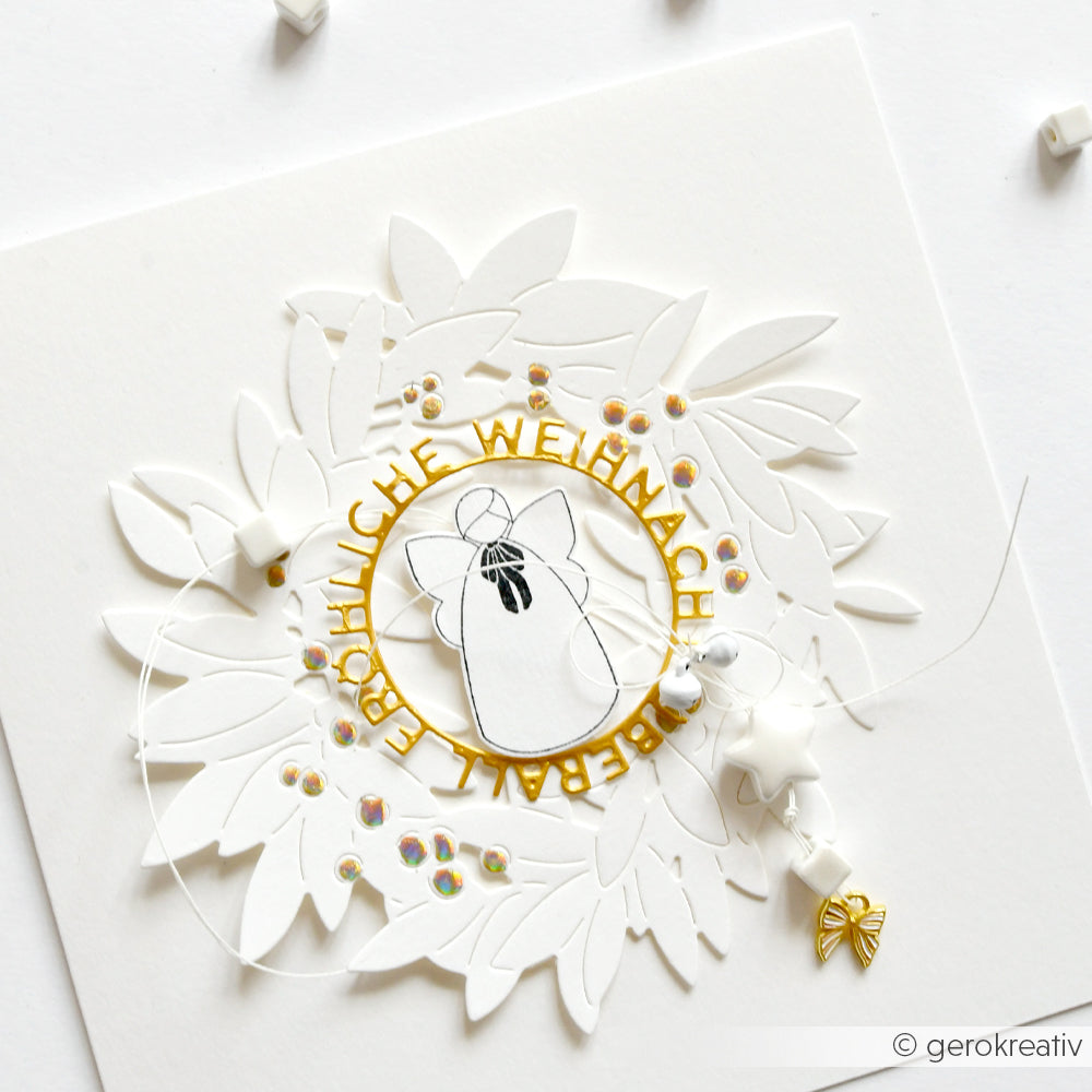 Weißer Papierkranz mit einer Glocke, goldenem Text und Perlen auf weißem Hintergrund, hergestellt mit Alexandra Renke Motivstanze Blätterkranz Dies für präzise Details.