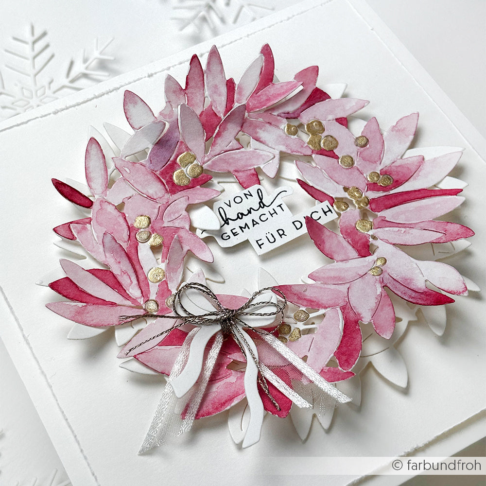 Eine rosafarbene und weiße Kranzkarte aus Alexandra Renke Designpapieren mit einer Schleife und einem deutschen Textetikett in der Mitte. Die zarten Details wurden mit der Alexandra Renke Motivstanze Blätterkranz hergestellt.