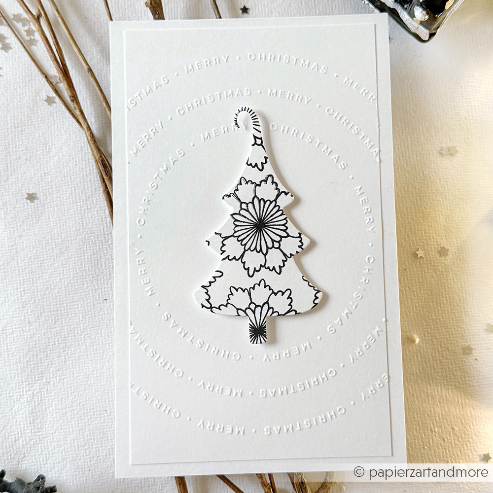 Weiße Karte mit einem schwarzen, floralen Weihnachtsbaum, gestaltet mit der Motivstanze Fröhliche Tanne von Alexandra Renke und den DieCut Systemen, umgeben von kreisförmig geprägtem Text Frohe Weihnachten. Ideal für festliche Designpapiere.