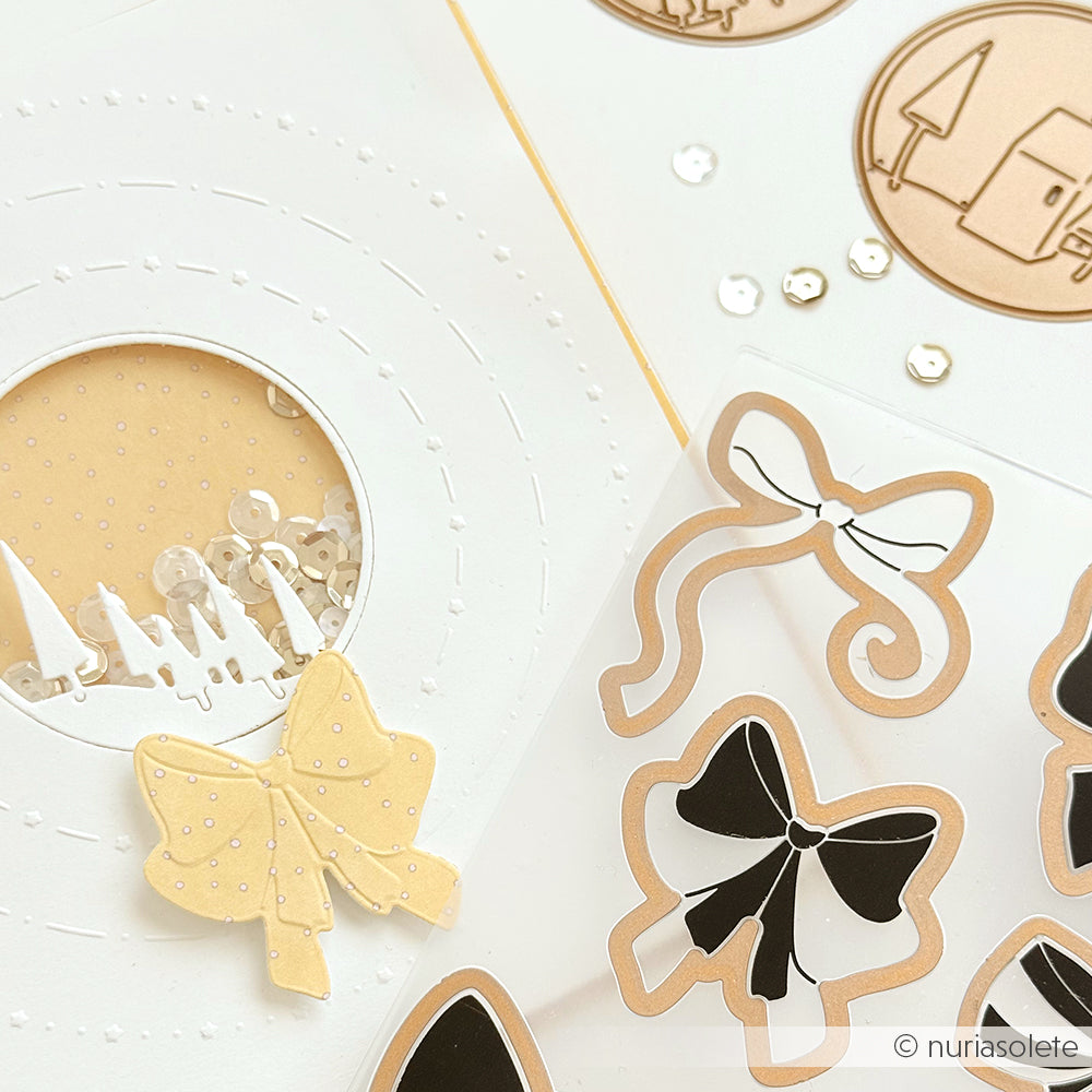 Papierausschnitte und Schleifenaufkleber auf einer weißen Fläche mit Pailletten, einer runden Fensterkarte und Akzenten - alles mit Alexandra Renke DieCut Systemen und Designpapieren erstellt.