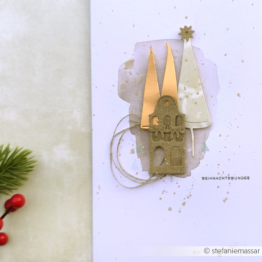 Handgefertigte Weihnachtskarte von Alexandra Renke mit goldenen Bäumen aus der Motivstanze Schiefe Tannen, einem Haus, Garn und dem Text "WEIHNACHTSWUNDER" auf weißem Designpapier.