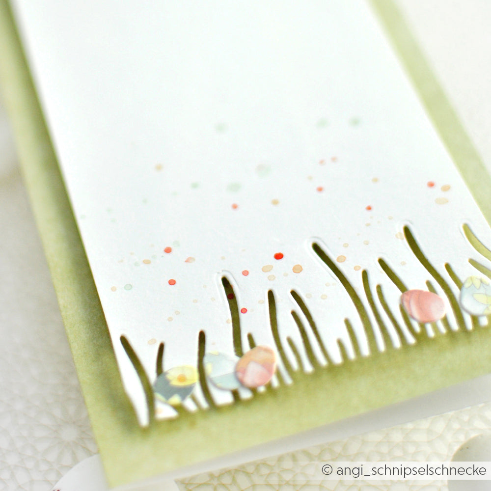 Eine weiße Alexandra Renke Karte mit Designpapieren und ausgeschnittenem Gras aus dem Motivstanze Grasbüschel-Set, das pastellfarbene Ostereier auf hellgrünem Hintergrund zeigt.