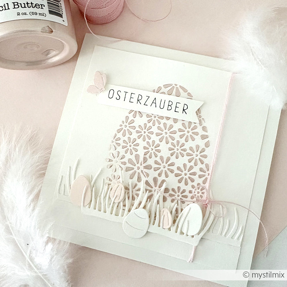 Handgefertigte Osterkarte von Alexandra Renke mit Spitzen-Ei, Motivstanze Grasbüschel, verzierten Eiern und "OSTERZAUBER" auf hochwertigen Designpapieren, alles vor weißem Hintergrund.