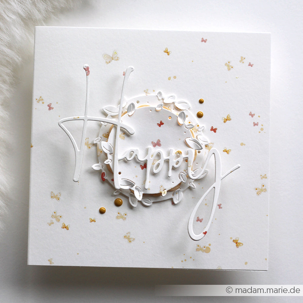 Weiße Karte mit "Happy" in eleganter Schrift, Schmetterlingen, goldenen Punkten und einem zarten Kranz - gestaltet mit Alexandra Renke Designpapieren und der Motivstanze Blättrige runde Aufleger für ein exquisites Finish.