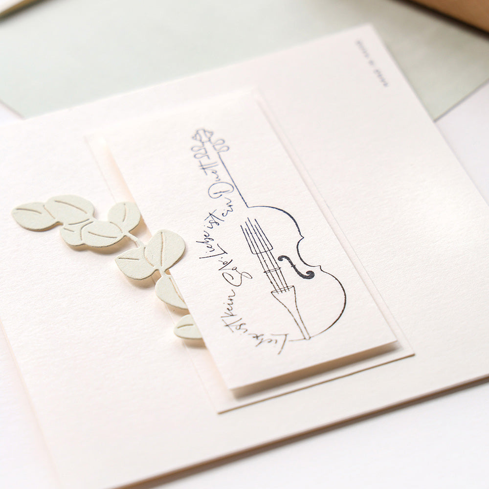 Eine Nahaufnahme einer Karte mit einer Geigenskizze, Noten und ausgeschnittenen Blättern aus Papier, hergestellt mit Alexandra Renke DieCut Systeme und Motivstanze Eukalyptuszweige auf weißem Hintergrund.