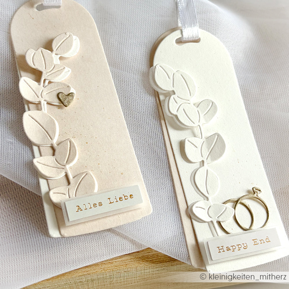 Zwei handgefertigte Lesezeichen mit geprägten Blättern - hergestellt mit Alexandra Renke Stanzen für Papier und einer Motivstanze Eukalyptuszweige - sowie kleine goldene Anhänger mit der Aufschrift "Alles Liebe" und "Happy End".
