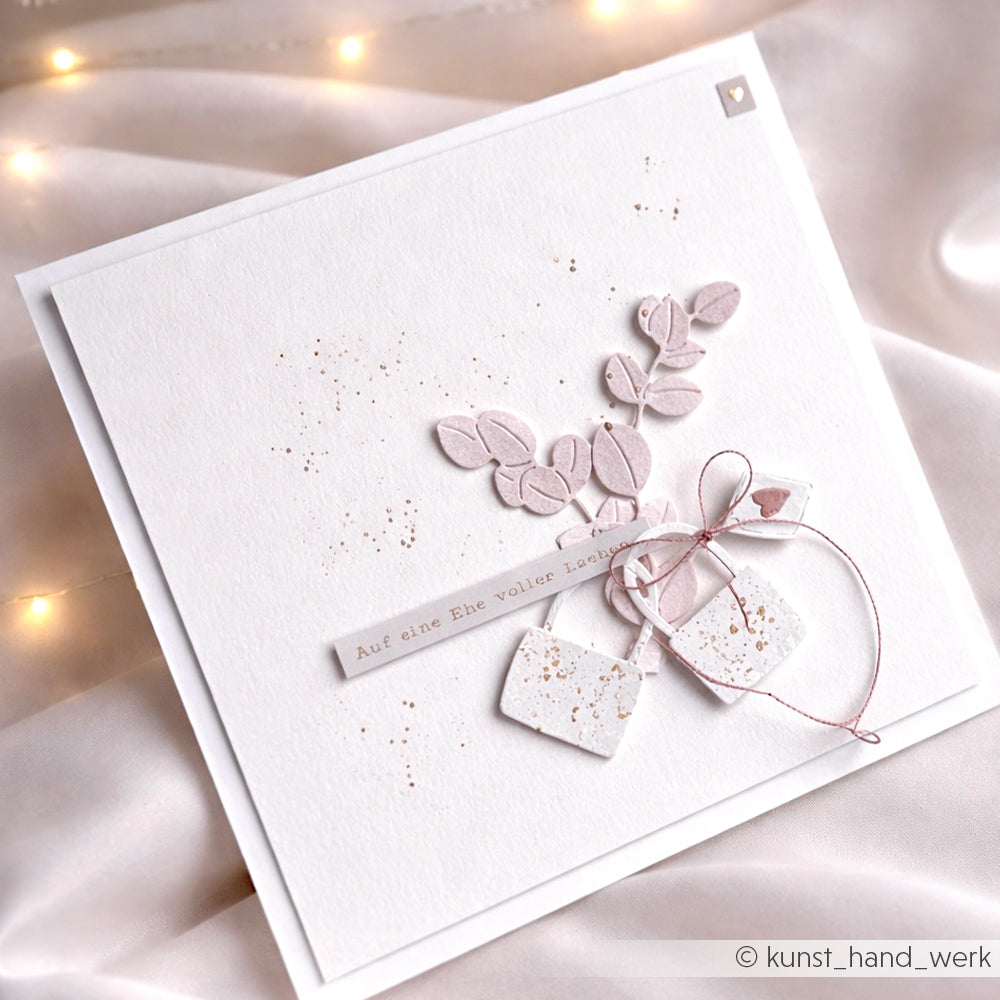 Quadratische weiße Alexandra Renke Grußkarte mit rosa Blättern, Anhängern und deutschem Text, verziert mit einer rosa Schleife, goldenen Sprenkeln und Eukalyptuszweige Dies-Akzenten auf hochwertigen Designpapieren.