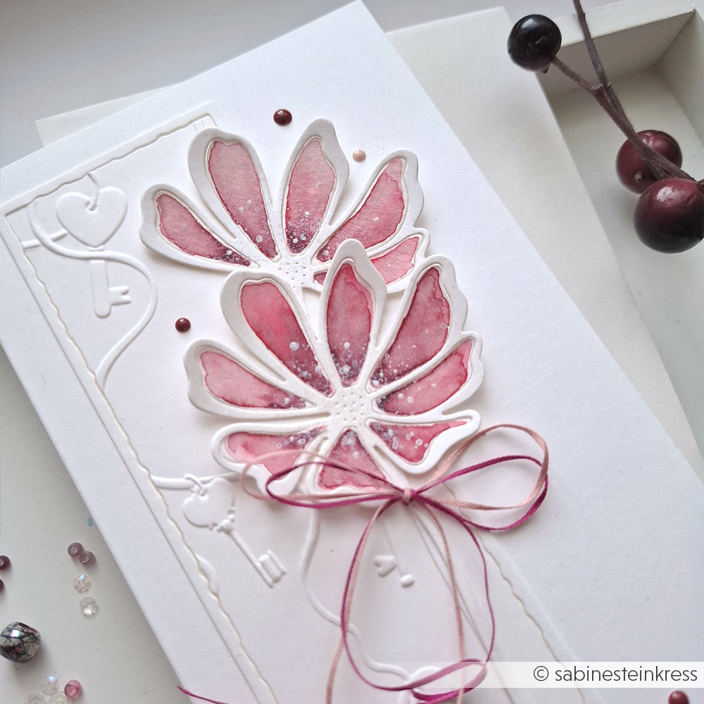 Handgefertigte Karte von Alexandra Renke mit zwei rosafarbenen Aquarellblumen, geprägten Details und einer Schleife, hergestellt mit Designpapiere und Motivstanze Gartenblume DieCut Systeme, neben Beeren und Pailletten.
