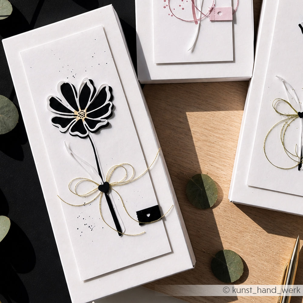 Elegante weiße Geschenkschachtel mit einem von Alexandra Renke's Motivstanze Lineart Gartenblume inspirierten schwarz-weißen Blumenmuster, goldenem Band und minimalistischer Dekoration.