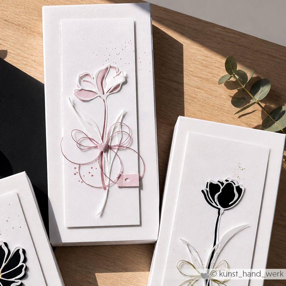 Drei elegante weiße Grußkarten von Alexandra Renke mit minimalistischen floralen Motiven, darunter die Lineart Fächerblumen, eine davon mit rosa Akzenten, werden auf einer Holzfläche präsentiert.