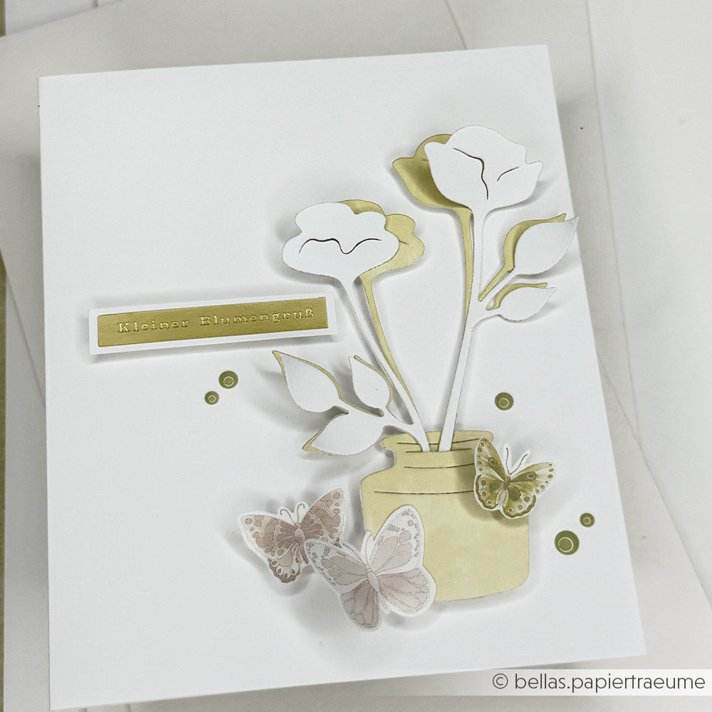 Handgefertigte Karte mit Papierblumen in einem Glas, Schmetterlingen, grünen Punkten und einem goldenen Etikett auf weißem Hintergrund, gestaltet mit der Motivstanze „Blütenpoesie“ von Alexandra Renke und hochwertigen Designpapieren für einen eleganten Touch.