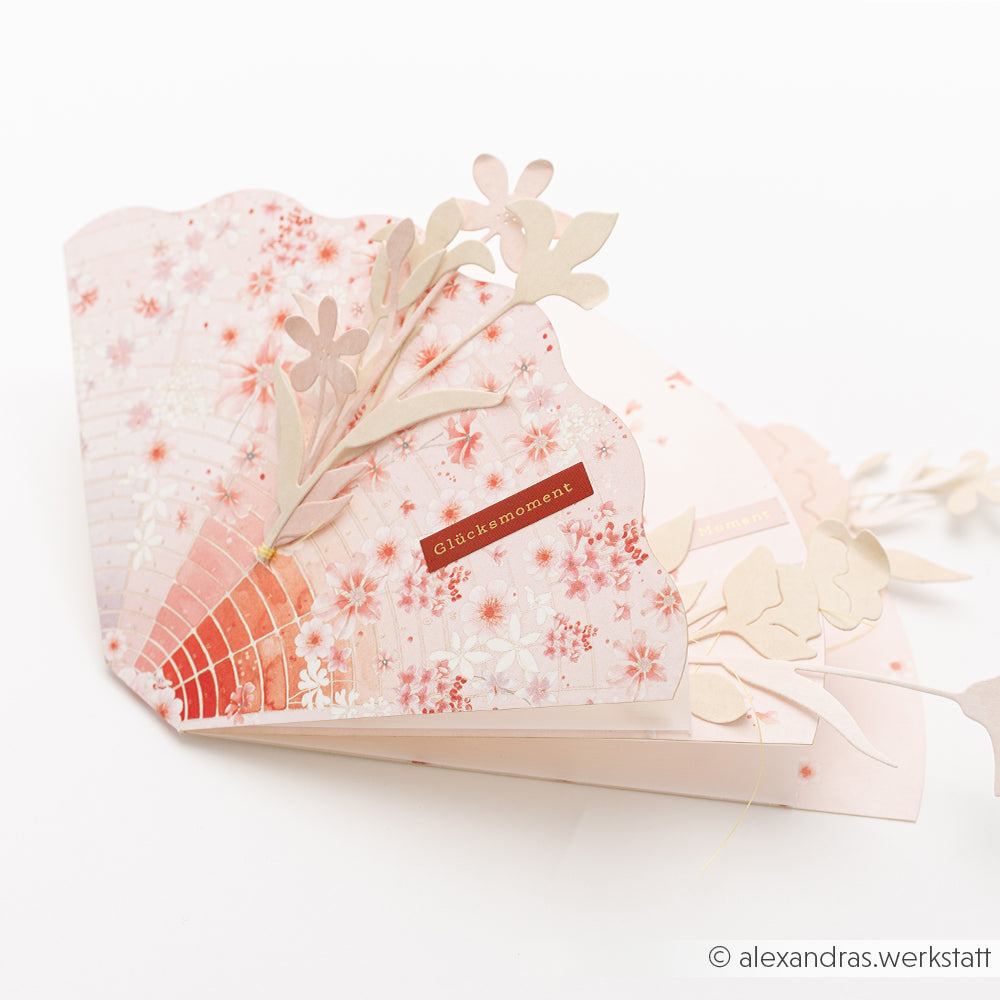 Eine handgefertigte, fächerförmige Blumenkarte von Alexandra Renke, hergestellt mit Motivstanze Zarte Blüten und elegantem Designpapier, verziert mit zarten ausgeschnittenen Blumen und einem "Glücksmoment"-Label.