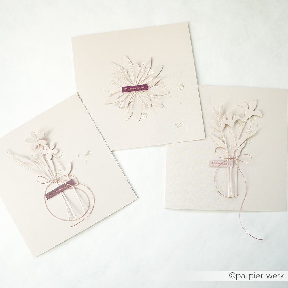 Drei elegante, beigefarbene Grußkarten von Alexandra Renke, gefertigt aus erlesenen Designpapieren mit Blumenmustern und mauvefarbenen Etiketten, die auf einem weißen Hintergrund angeordnet sind.