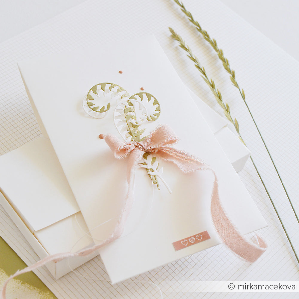 Weiße Karte mit einer rosa Schleife, zarten Papierblättern, die mit der Motivstanze „Farn Paar“ gestaltet wurden, und winzigen Herzchen, die auf einer weißen, strukturierten Oberfläche angeordnet sind.