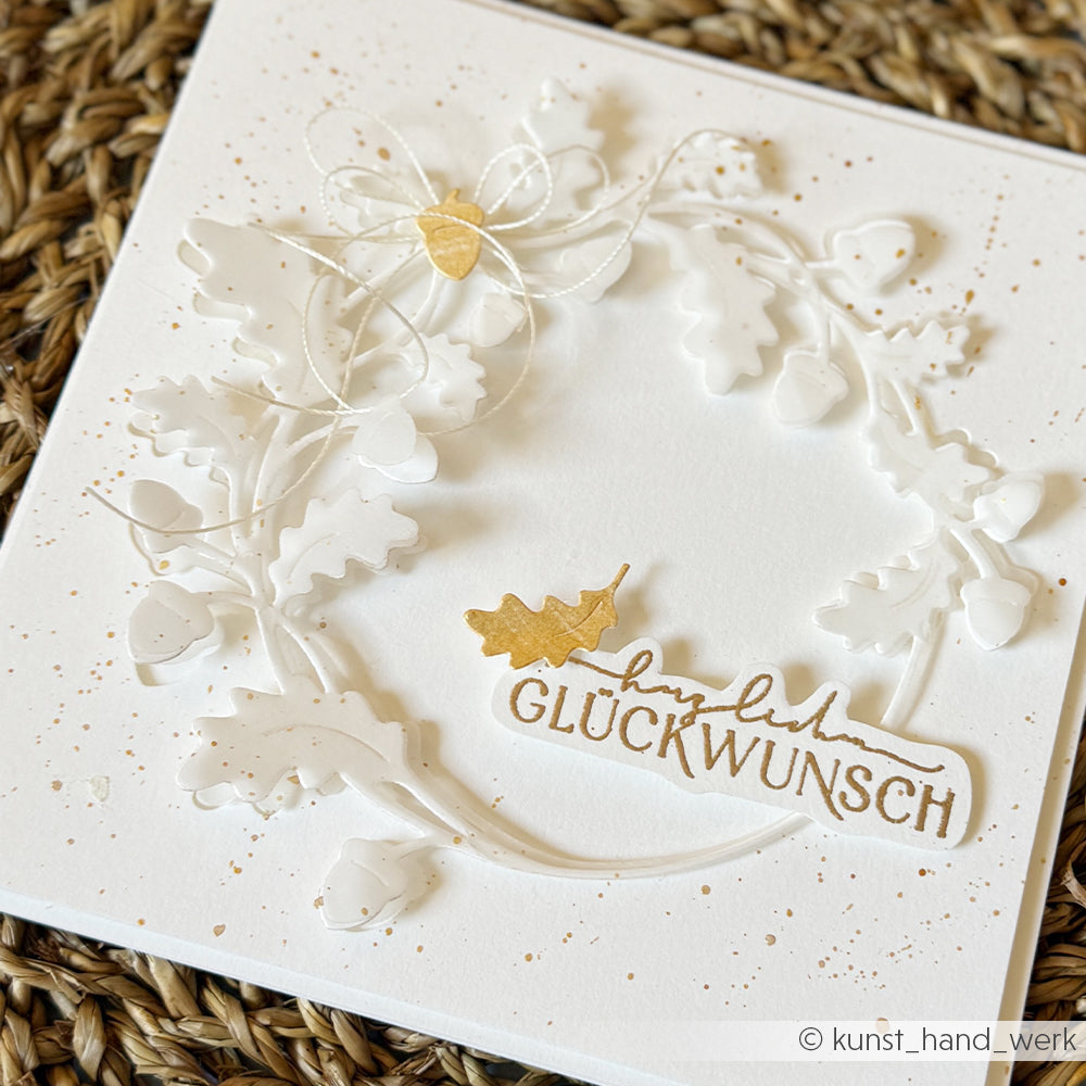 Weiße Grußkarte aus edlem Designpapier mit erhabenen Eichenblättern und Eicheln, die mit dem Motivstanz-System „Eichenkranz“ gestaltet wurden. Akzentuiert mit Blattgold und dem Schriftzug „Herzlichen Glückwunsch“ in eleganter goldener Schreibschrift.