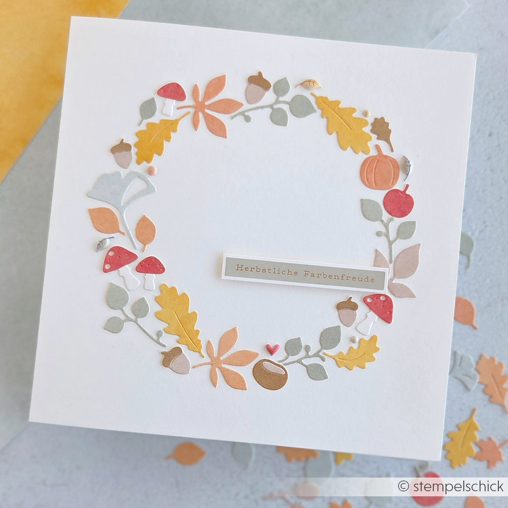 Quadratische Karte mit einem Kranz aus Herbstblättern, Pilzen, einem Kürbis und einem Schriftzug mit der Aufschrift „Herbstliche Farbenfreude“ – gefertigt mit Stanzsystemen und Designpapieren für exquisite saisonale Details.