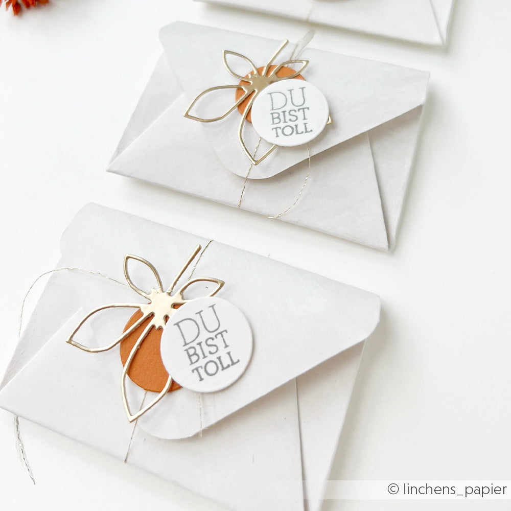 Weiße Umschläge, verziert mit Blumen aus Golddraht und Anhängern mit der Aufschrift „DU BIST TOLL“ auf weißem Hintergrund, mit zarten Akzenten, die mit der Motivstanze „Blätterwirbel“ und hochwertigen Designpapieren gestaltet wurden und für einen wahrhaft eleganten Touch sorgen.
