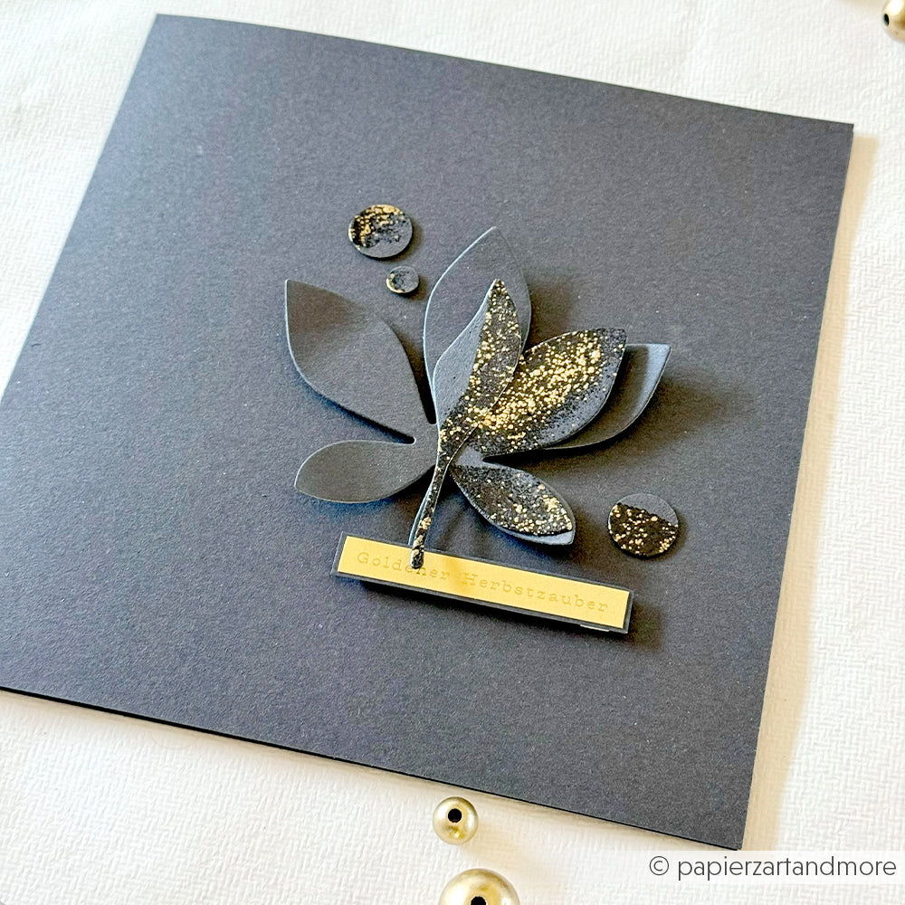 Handgefertigte schwarze Karte mit einem glitzernden 3D-Blattmotiv, hergestellt aus hochwertigen Designpapieren und mit einer Motivstanze aus dem Kastanien-Set, abgerundet durch ein kleines goldenes Etikett am unteren Rand.