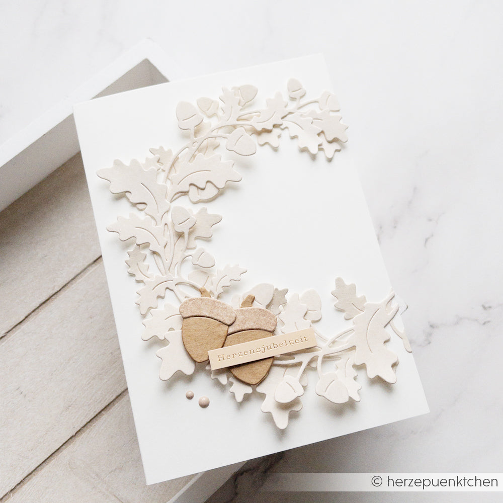 Weiße Grußkarte aus eleganten Designpapieren, verziert mit erhabenen Eichenblättern, die mit der Motivstanze „Eichenblatt“ gestanzt wurden, zwei Holzherzen und einem kleinen „Herzensjubelzeit“-Etikett.