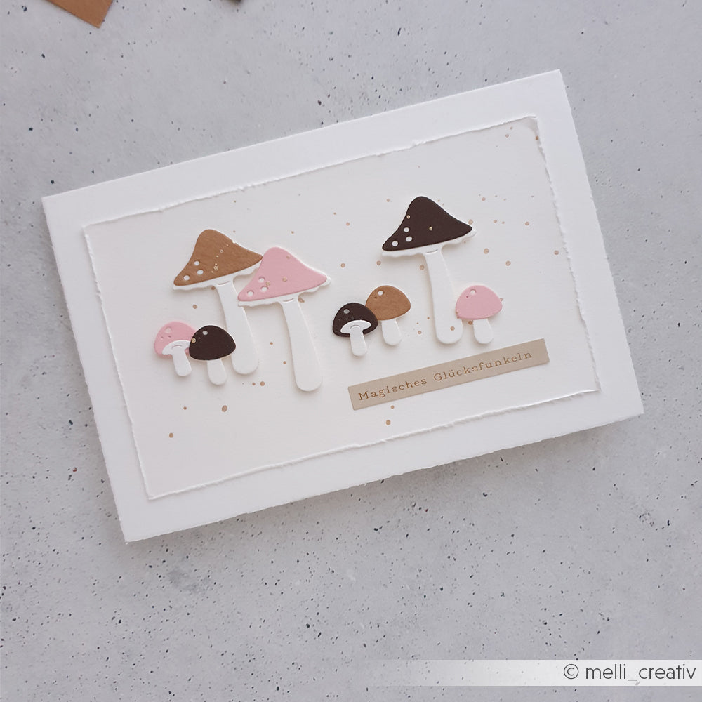 Handgefertigte Karte mit rosa und braunen Pilzmotiven, die mit der Motivstanze „Kleines Pilz Trio“ gestaltet wurden, sowie dem Schriftzug „Magisches Glücksfunken“ auf weißem Papier, wunderschön gefertigt aus hochwertigen Designpapieren.