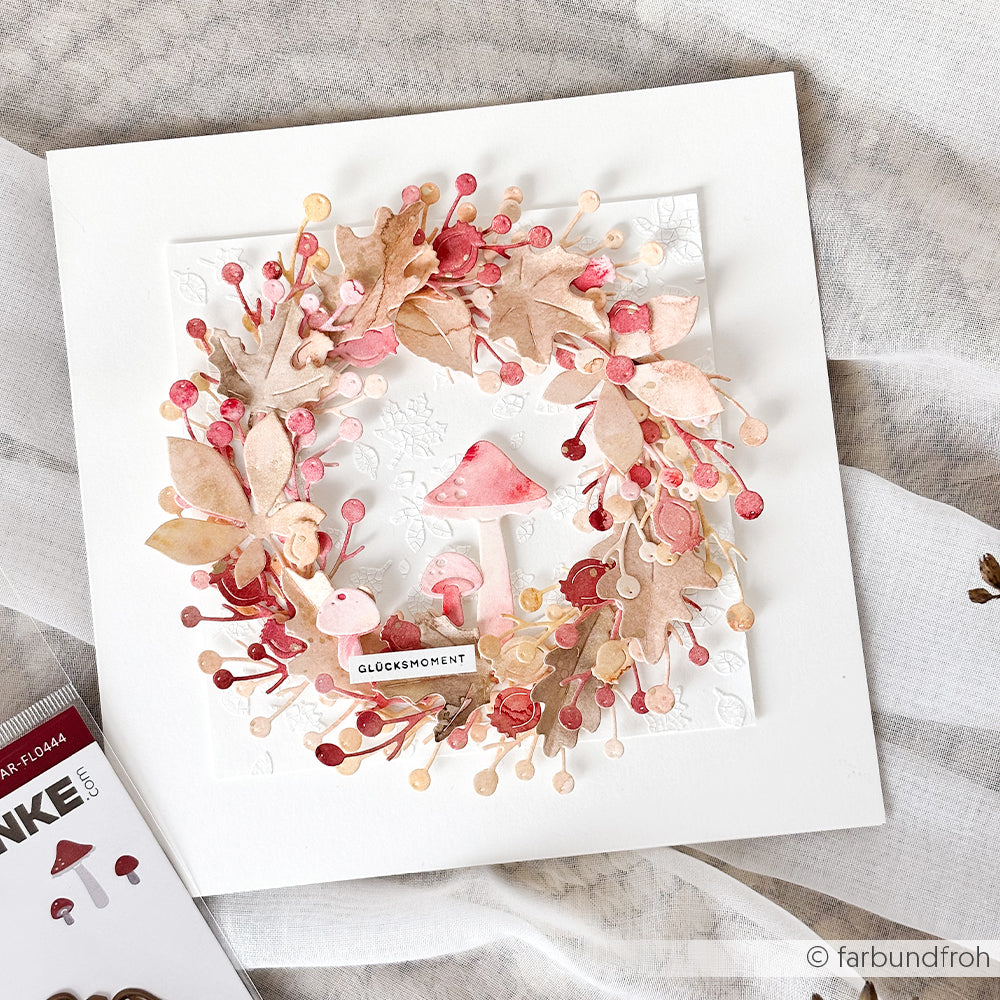 Handgefertigte Karte mit einem Kranz aus rosa und braunen Blättern, Beeren und Pilzen auf weißem Hintergrund, wunderschön gestaltet mit Designpapieren und verziert mit zarten Details aus dem Stanzset „Zierzweige“ von DieCut Systeme.