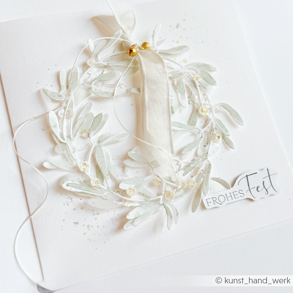 Weihnachtskarte mit einem Mistelzweigkranz aus Papier, gestaltet mit einer Motivstanze, und dem Text FROHES FEST.