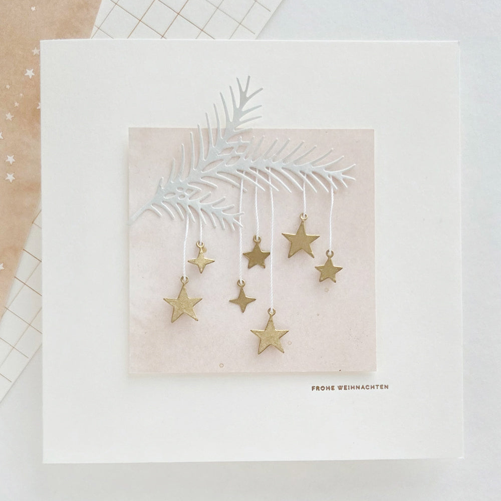 Eine quadratische Weihnachtskarte mit einer Illustration von Tannenzweigen und hängenden goldenen Sternen als Christbaumschmuck, mit der Aufschrift „FROHE WEIHNACHTEN“.