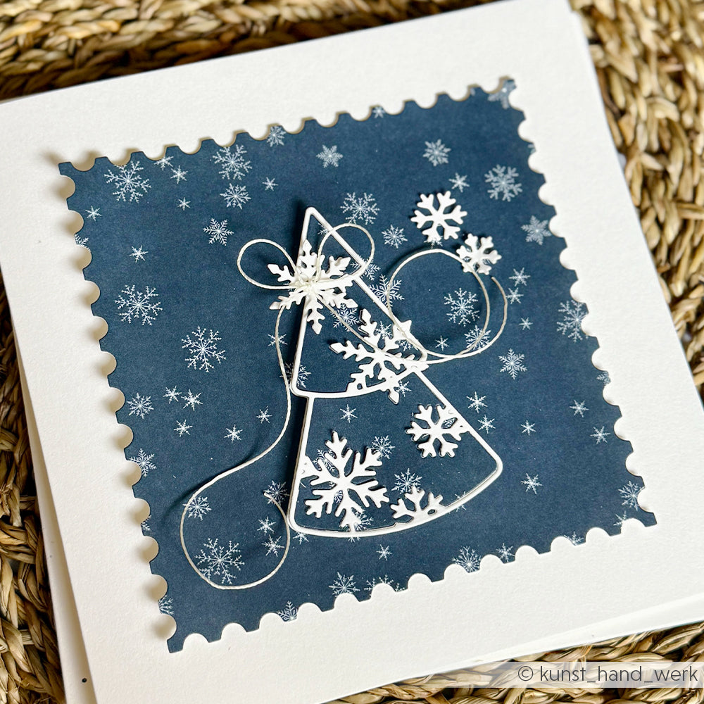 Handgefertigte Grußkarte mit dem Umriss eines Weihnachtsbaums aus Papier, verziert mit weißen Schneeflocken auf marineblauem Hintergrund.
