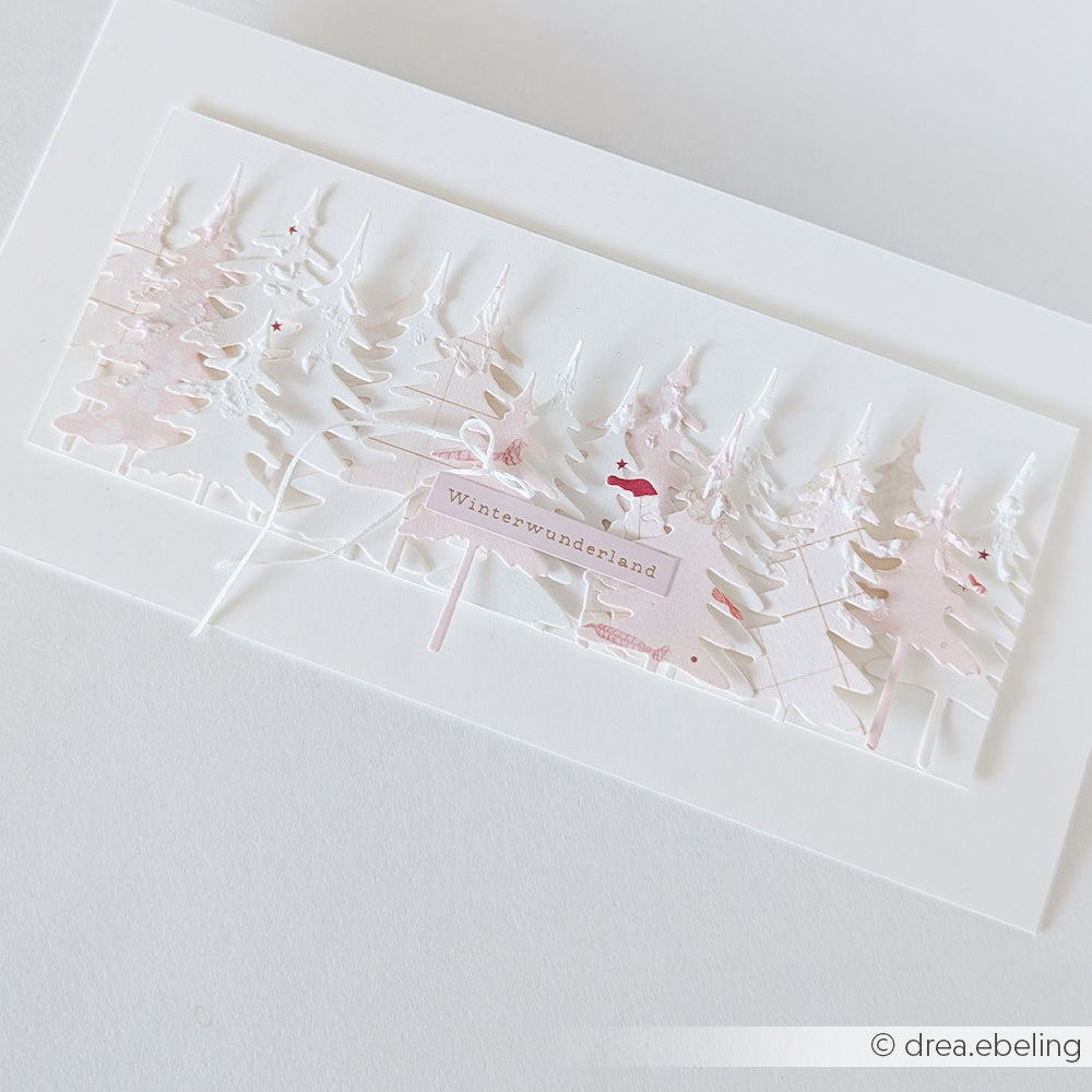 Handgefertigte Karte mit mehrschichtigen Papier-Tannenbäumen, gestaltet mit den Stanzformen Kleine Tannen und Winterwunderland von Motivstanze.
