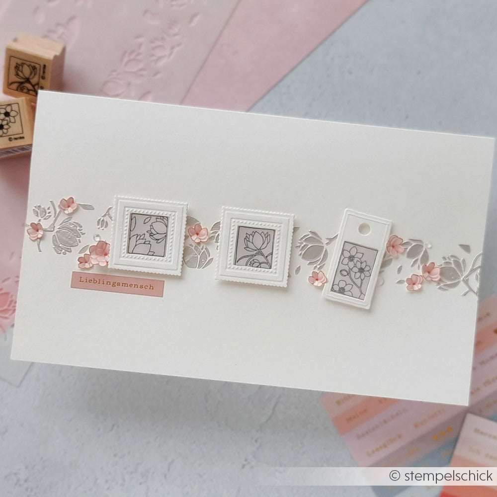 Eine handgefertigte Karte von Alexandra Renke mit floralen Motiven mit kleinen rosafarbenen Blumen, drei gerahmten Blumenbildern in der Mitte und zarten Blütenornamenten, die mit einem Holzstempel erstellt wurden.