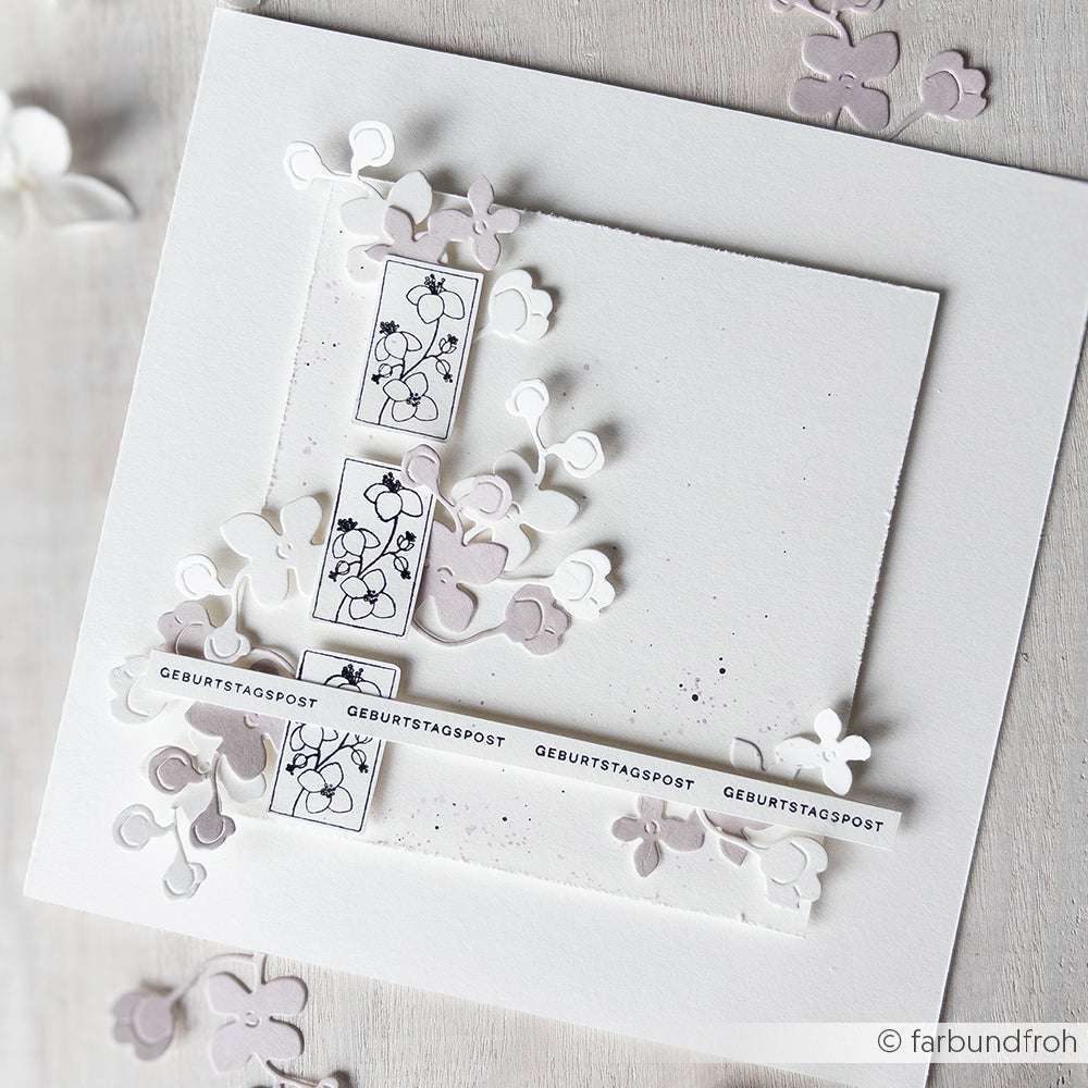 Quadratische weiße Karte von Alexandra Renke mit zarten Blütenornamenten, dekorativen Stempelgummi-Stempeln und dem Text "Geburtstagspost" auf weißen Streifen.